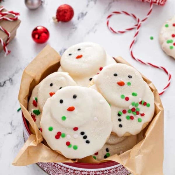 Melted snowman cookies in a festive holiday tin, set on a marble countertop.