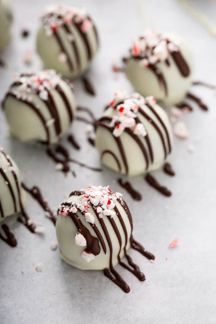 Peppermint oreo balls decorated in white candy melts with chocolate drizzle and crushed candy canes arranged on a parchment-lined baking sheet