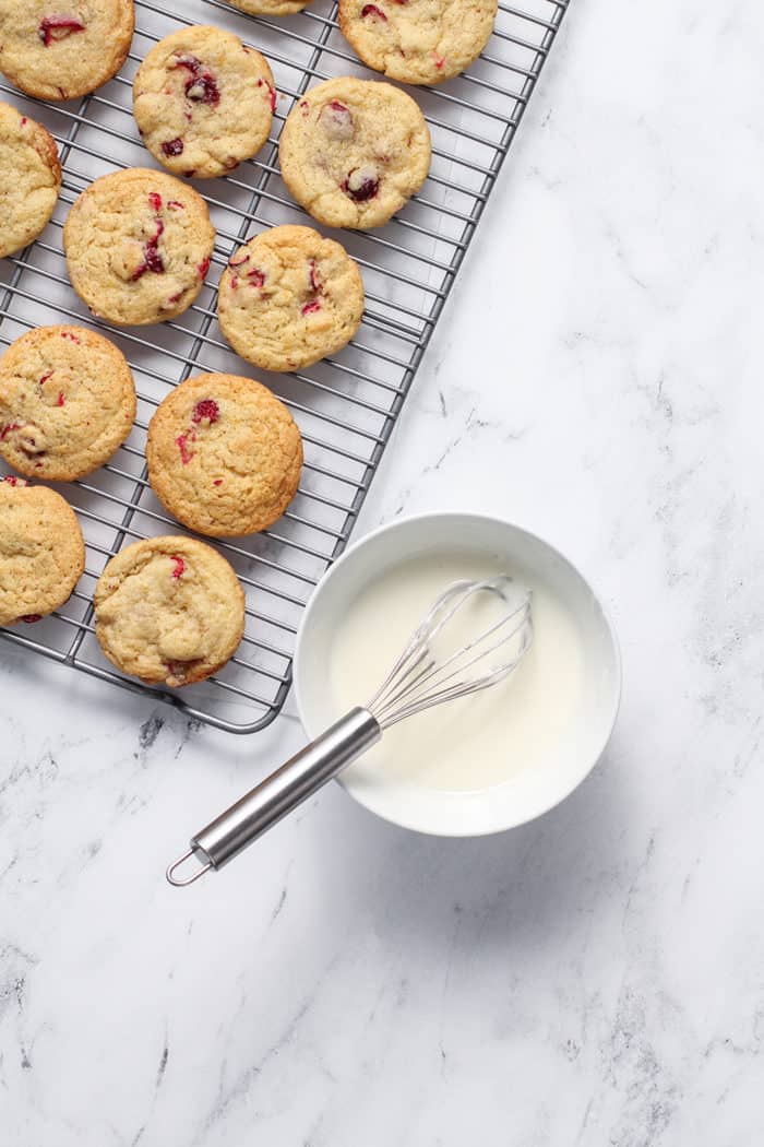 Wire rack of cooling orange cranberry cookies next to a bowl of icing