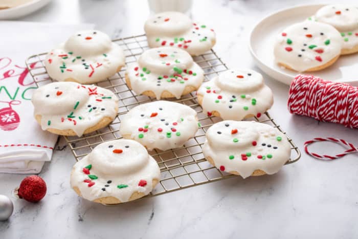 Melted snowman cookies on a wire rack, with a plate of cookies in the background.