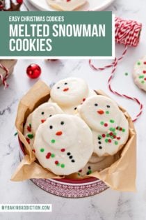 Melted snowman cookies in a festive holiday tin, set on a marble countertop. Text overlay includes recipe name.