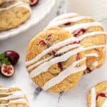 Orange cranberry cookies drizzled with icing on a marble countertop next to a glass of milk