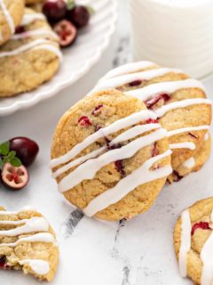 Orange cranberry cookies drizzled with icing on a marble countertop next to a glass of milk