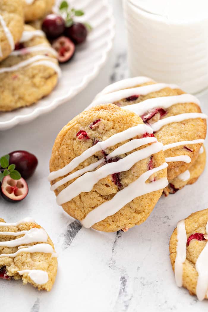 Orange cranberry cookies drizzled with icing on a marble countertop next to a glass of milk