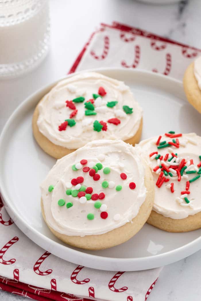 Three sour cream sugar cookies, topped with Christmas sprinkles, on a white plate.