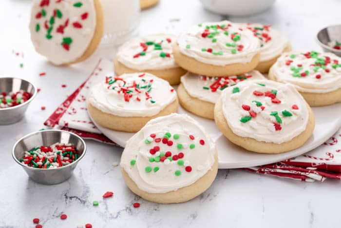 Assortment of sour cream sugar cookies, topped with red and green sprinkles, arranged on a white platter.