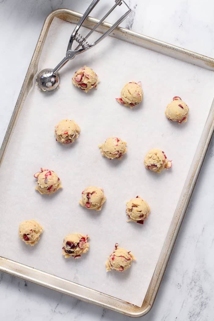 Orange cranberry cookie dough portioned out onto a parchment-lined baking sheet