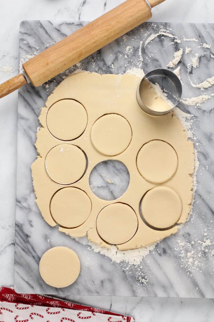 Dough for sour cream cookies rolled out on a marble slab and cut into circle shapes.