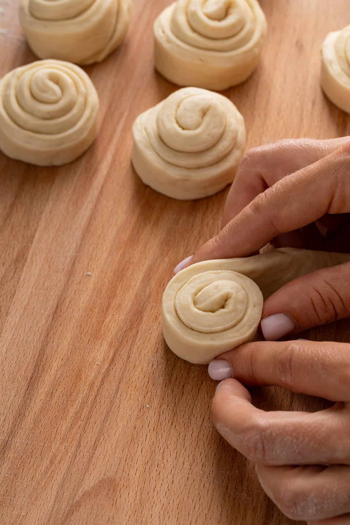 Person rolling dough strip into a curlicue roll.