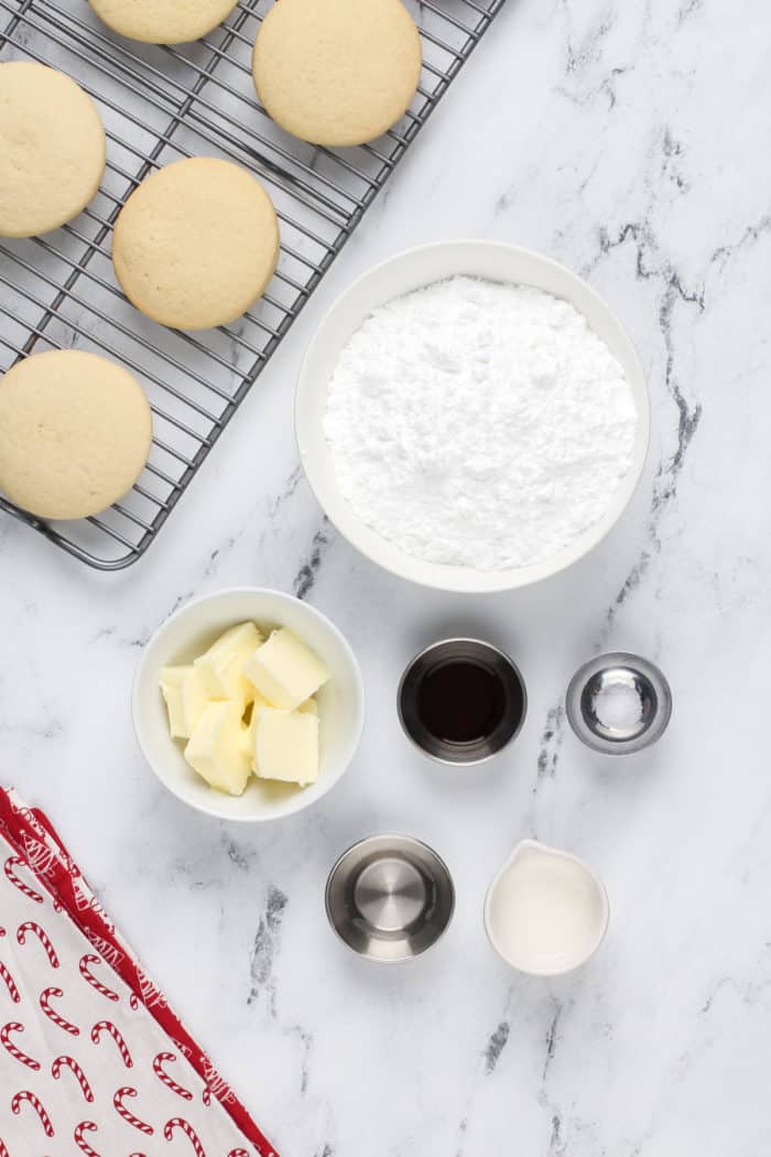 Ingredients for frosting to accompany sour cream cookies arranged on a marble countertop.