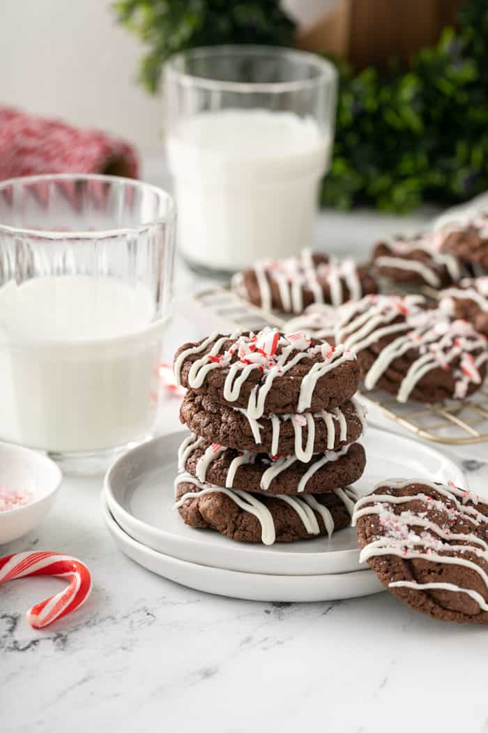 Four peppermint mocha cookies stacked on a plate. Glasses of milk and more cookies are in the background