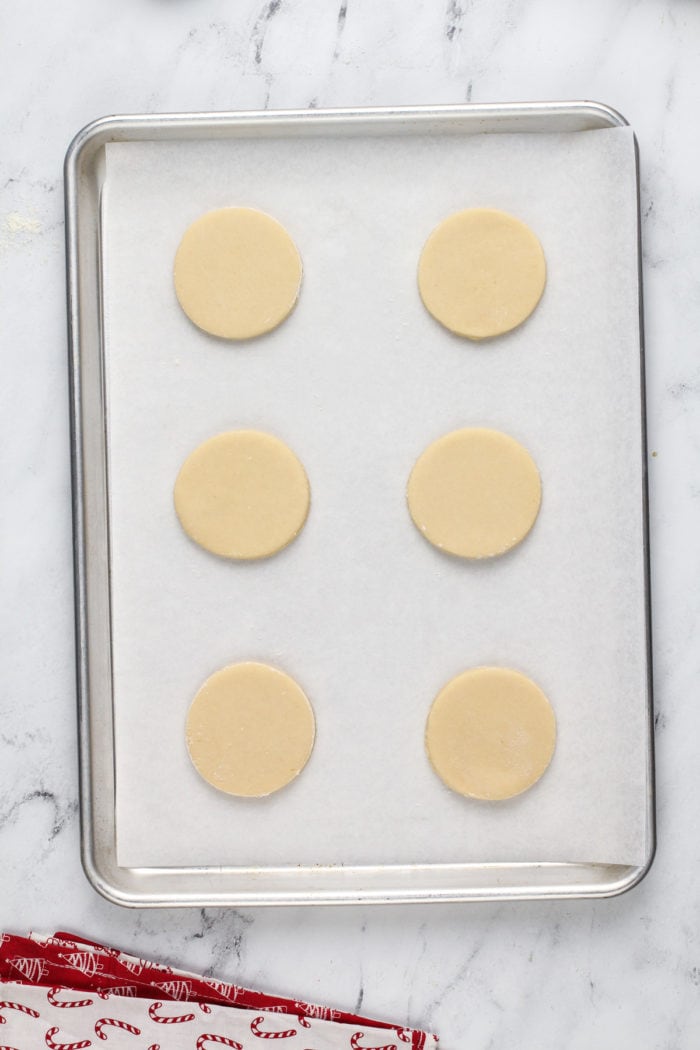 Six unbaked sour cream sugar cookies on a parchment-lined baking sheet.