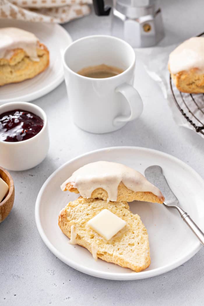 Vanilla bean scone cut in half on a plate. A pat of butter is on the bottom half of the scone.