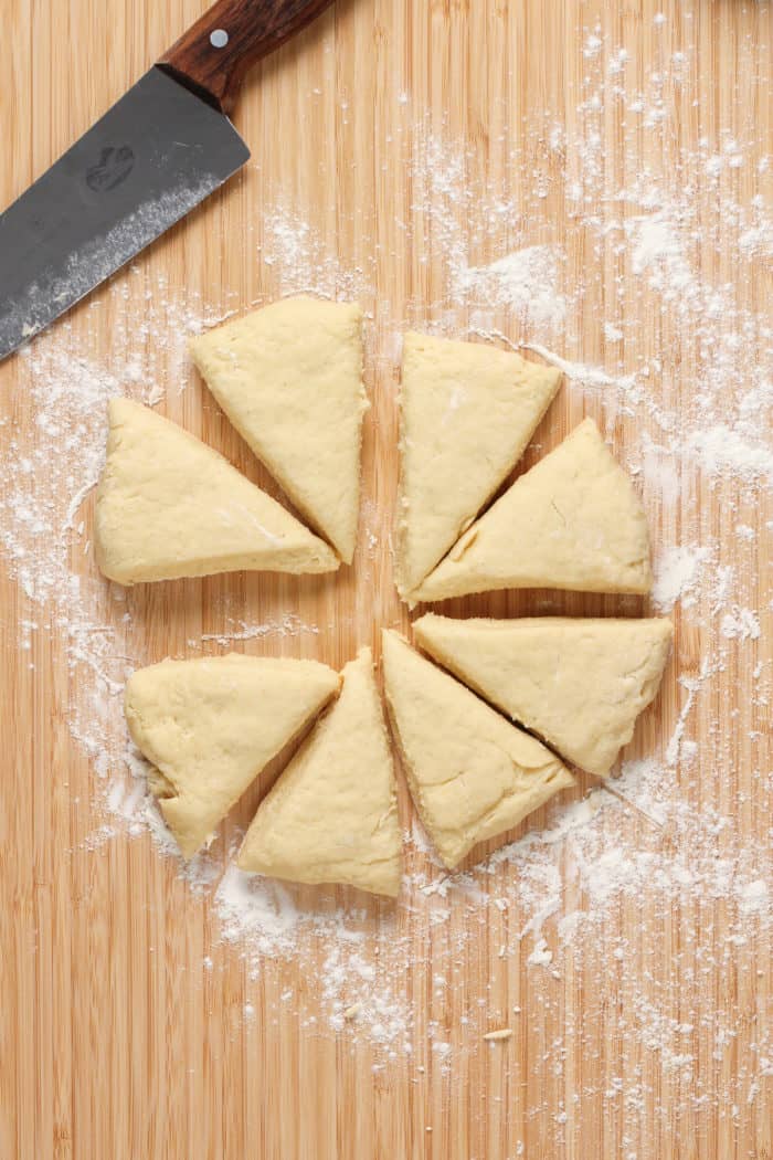 Vanilla bean scone dough cut into 8 triangles on a floured cutting board.