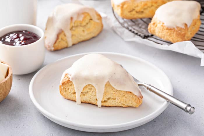 Vanilla bean scone topped with vanilla glaze set on a white plate with more scones in the background.