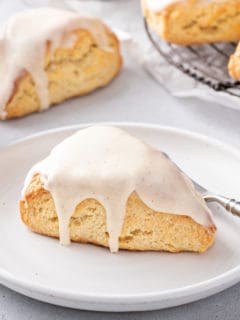 Glazed vanilla bean scone set on a white plate next to a fork.