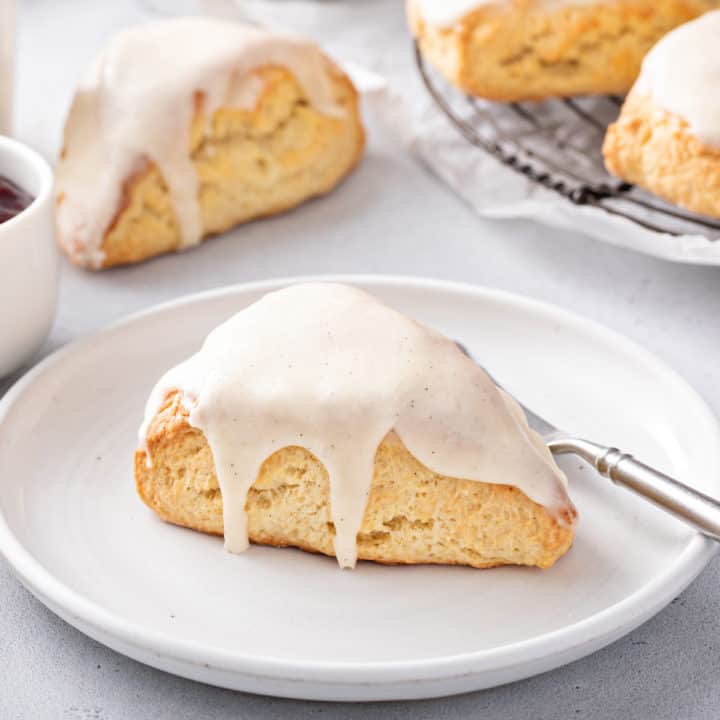 Glazed vanilla bean scone set on a white plate next to a fork.