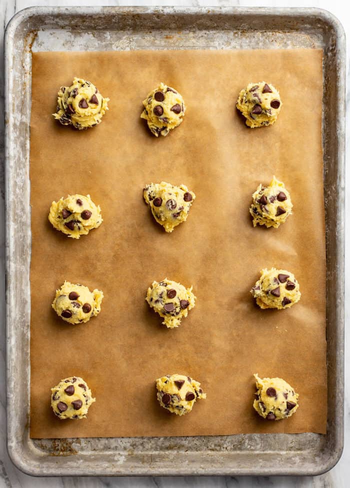 Portioned balls of chocolate chip pudding cookie dough on a parchment-lined baking sheet, ready to bake