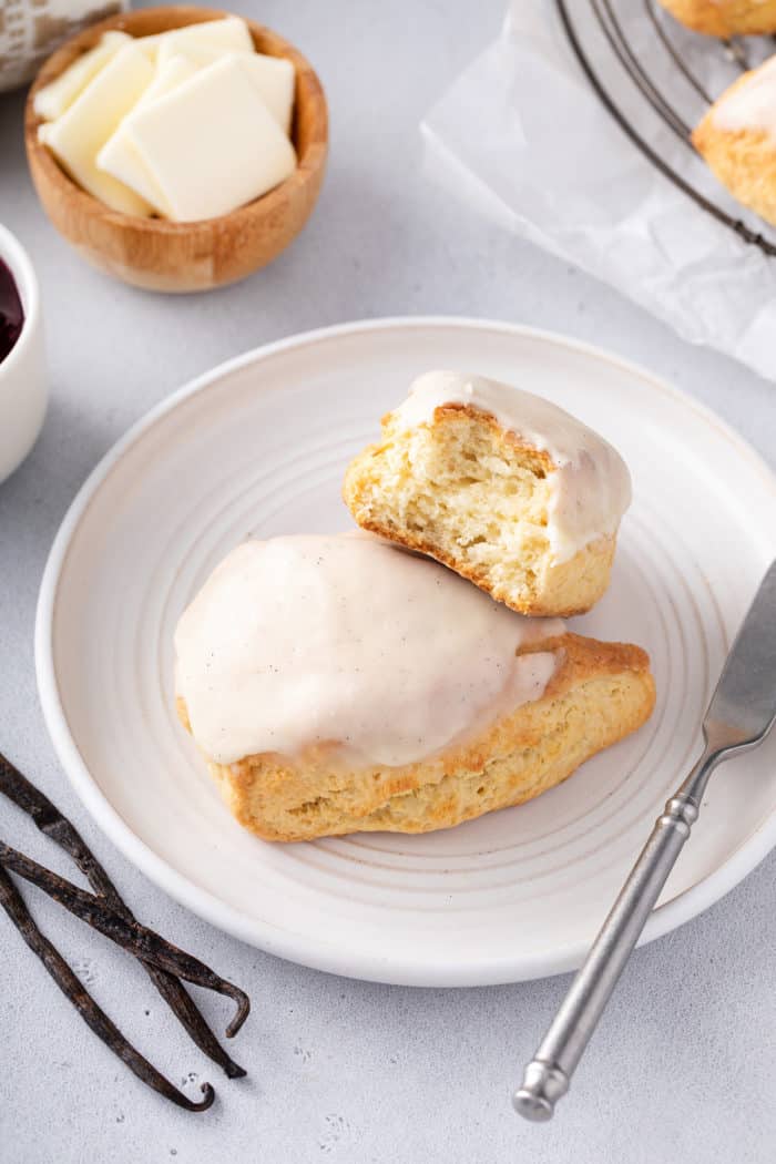 Two vanilla bean scones on a white plate. One of the scones is broken in half to show the light texture inside.