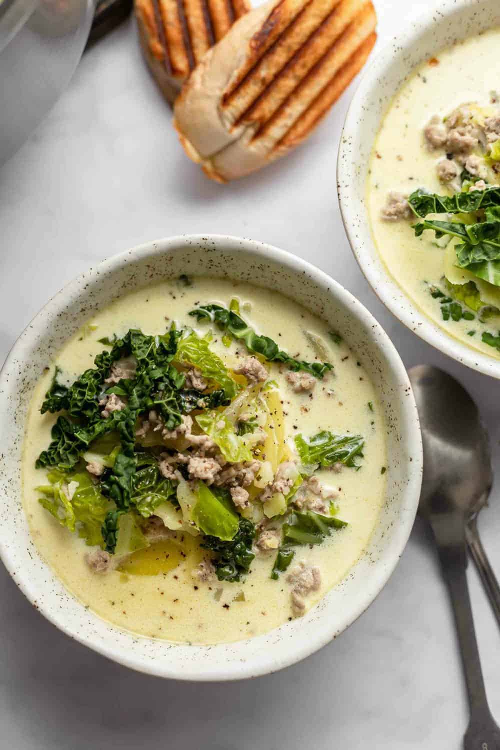 Zuppa toscana in white bowls next to grilled bread