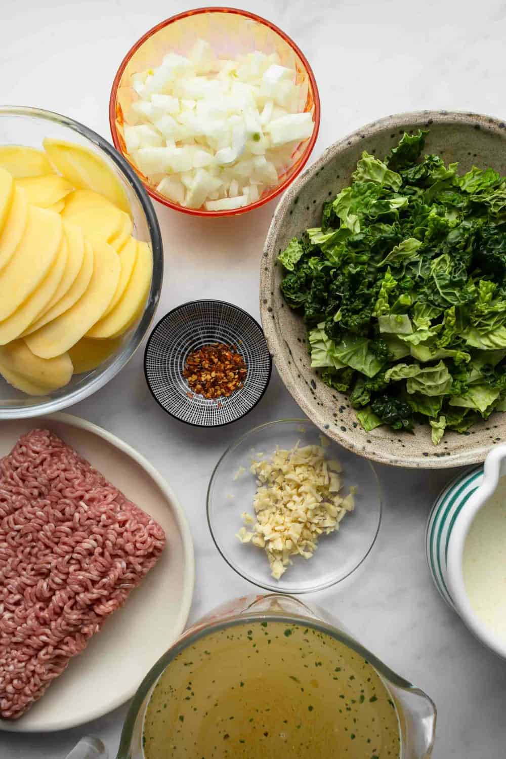 Ingredients for zuppa toscana in prep bowls on a marble surface