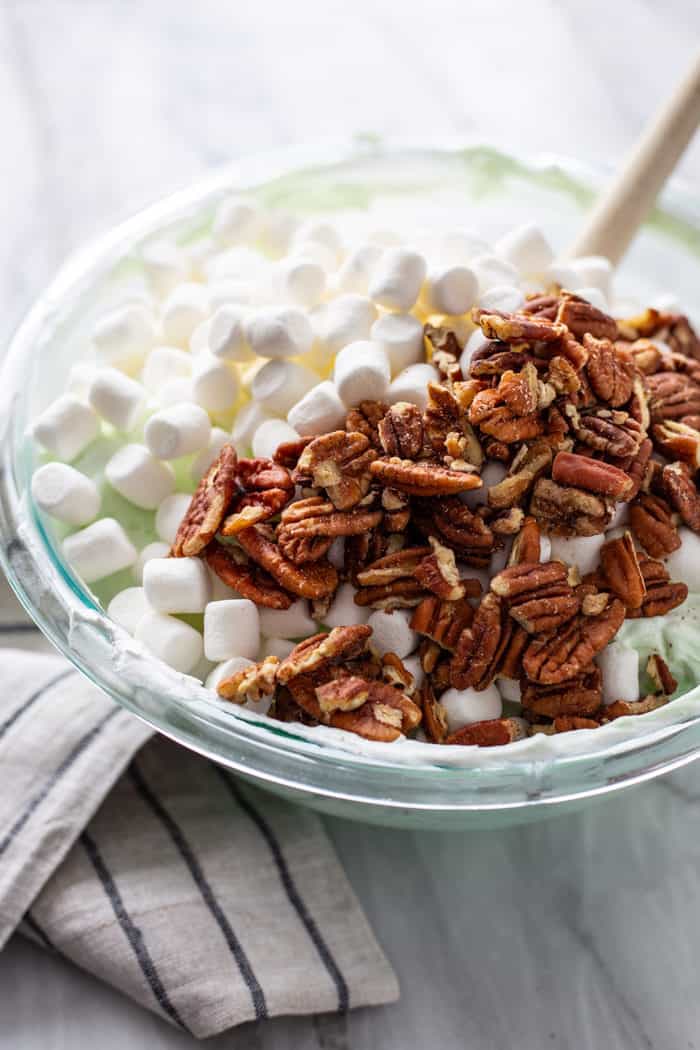 Pecans and mini marshmallows being added to a bowl of watergate salad