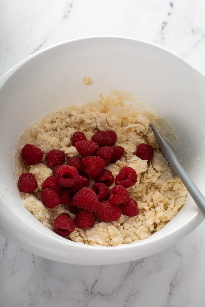 Raspberries about to be stirred into dough for lemon raspberry scones in a white mixing bowl