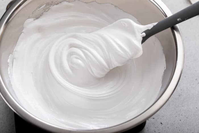 Spatula stirring homemade marshmallow frosting in a metal mixing bowl.