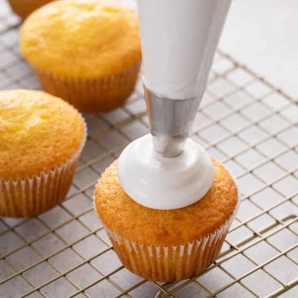 Piping bag piping marshmallow frosting onto a vanilla cupcake.