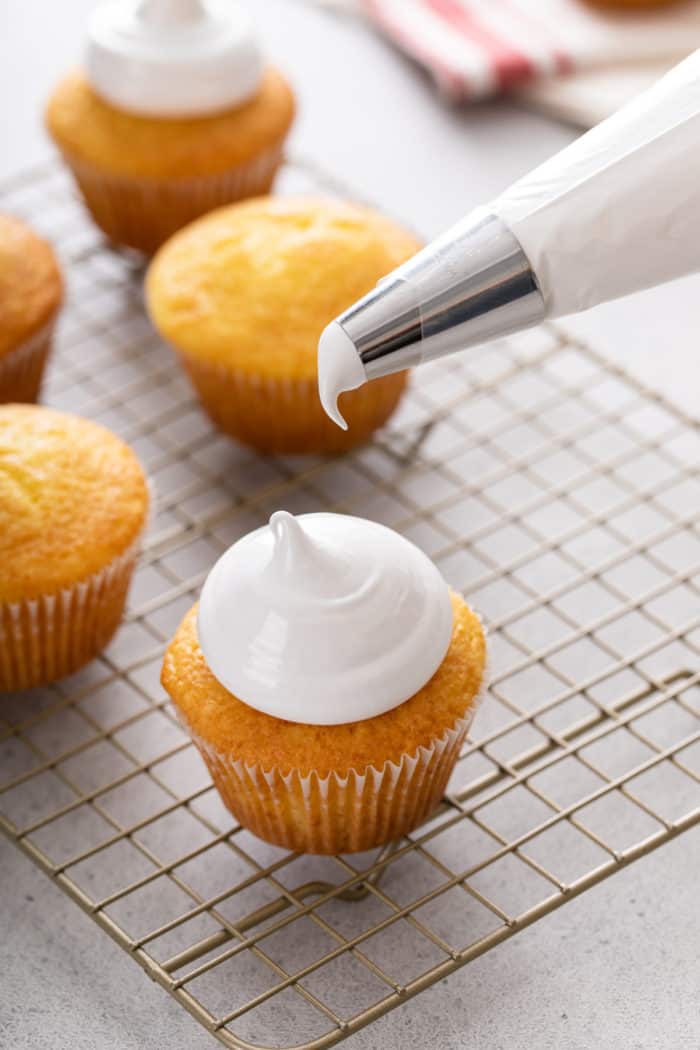 Cupcake topped with marshmallow frosting with the piping bag just over the top of the cupcake.