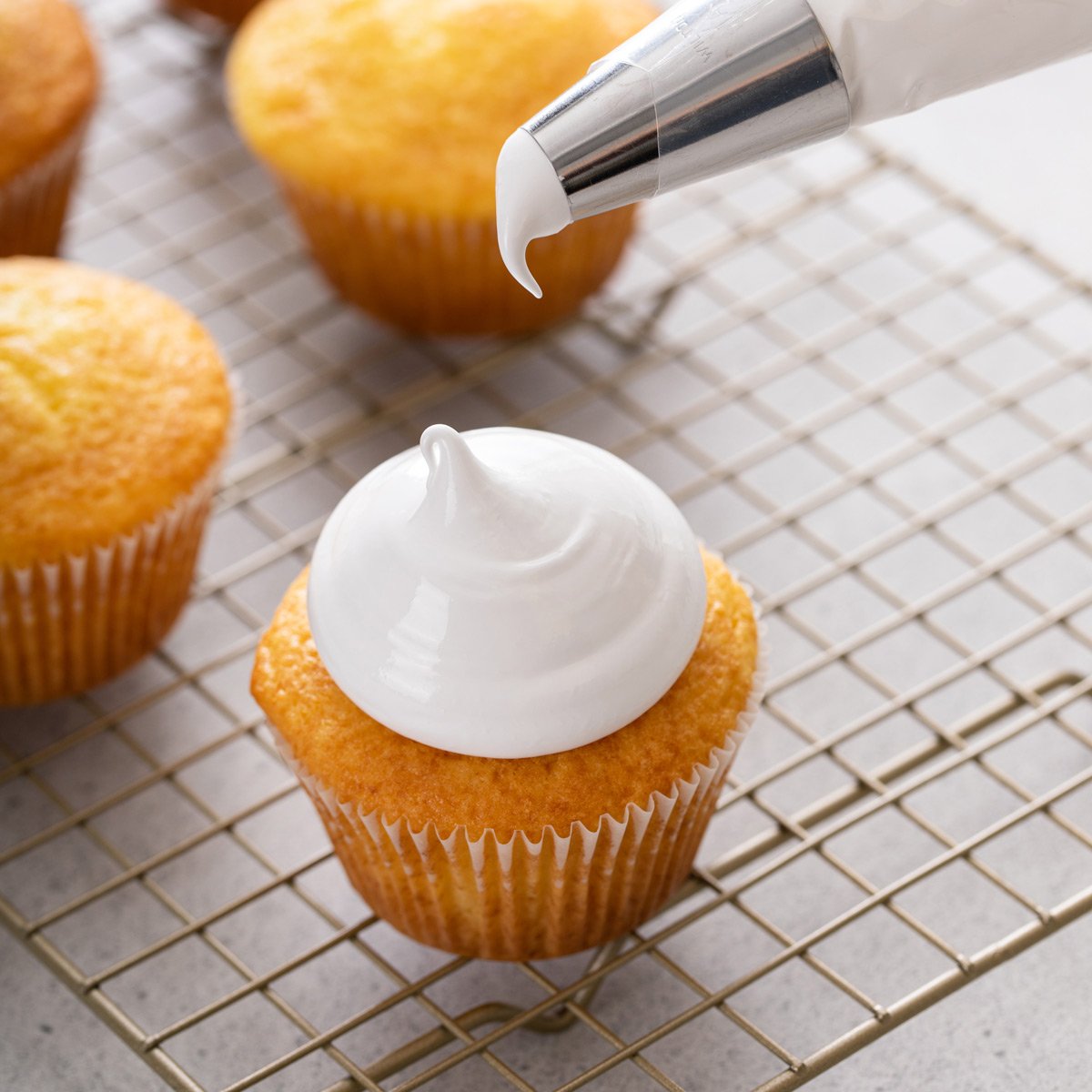 Piping bag held just above a cupcake topped with homemade marshmallow frosting.