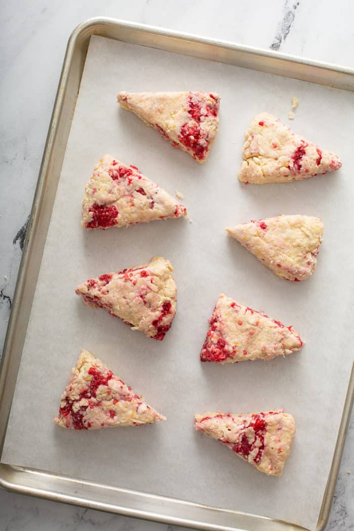 Lemon raspberry scone dough cut into triangles and arranged on a parchment-lined baking sheet for baking