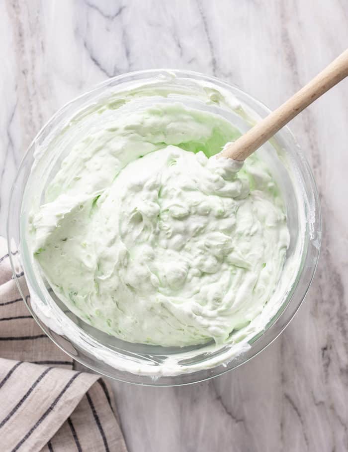 Spatula folding together whipped topping with pineapple and pistachio pudding mix