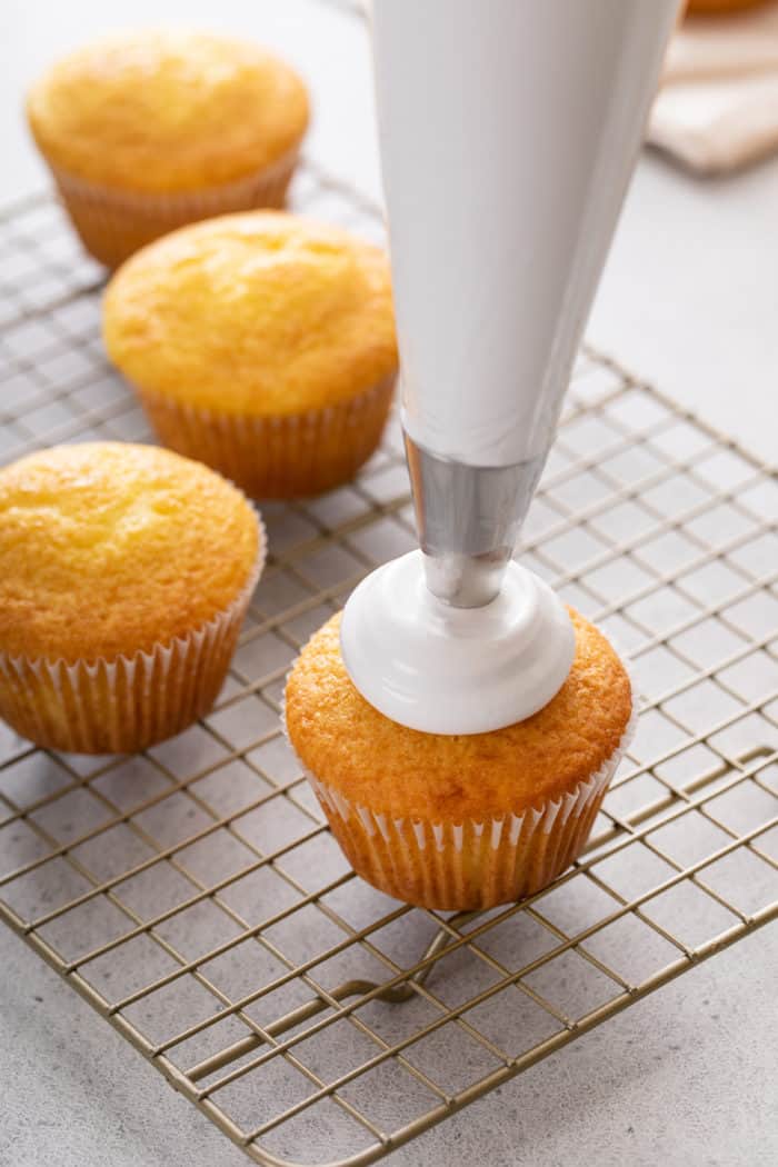 Piping bag piping marshmallow frosting onto a vanilla cupcake.