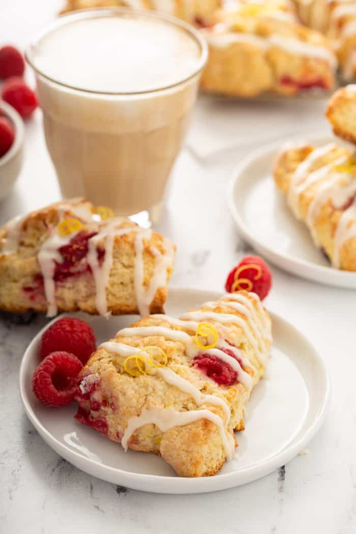 Lemon raspberry scones on white plates next to a glass of iced coffee