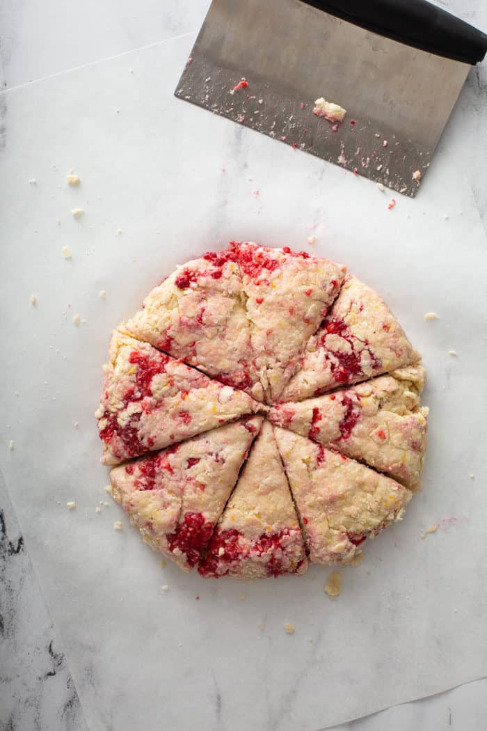Lemon raspberry scone dough formed into a circle and cut into 8 triangles on a marble surface