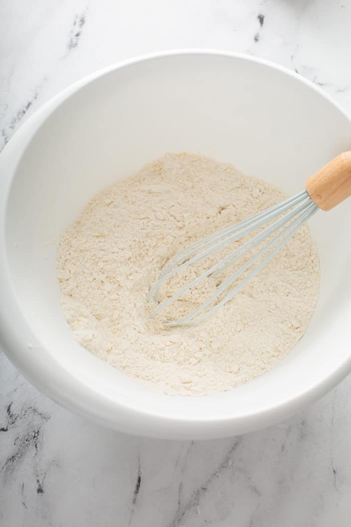 Whisk stirring together dry ingredients for lemon raspberry scones in a white mixing bowl