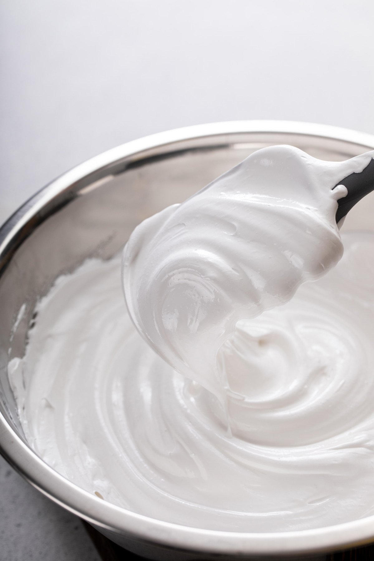 Spatula holding up a big dollop of marshmallow frosting over a bowl of the frosting.