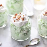 Watergate salad in four small serving dishes, topped with whipped cream and chopped pecans