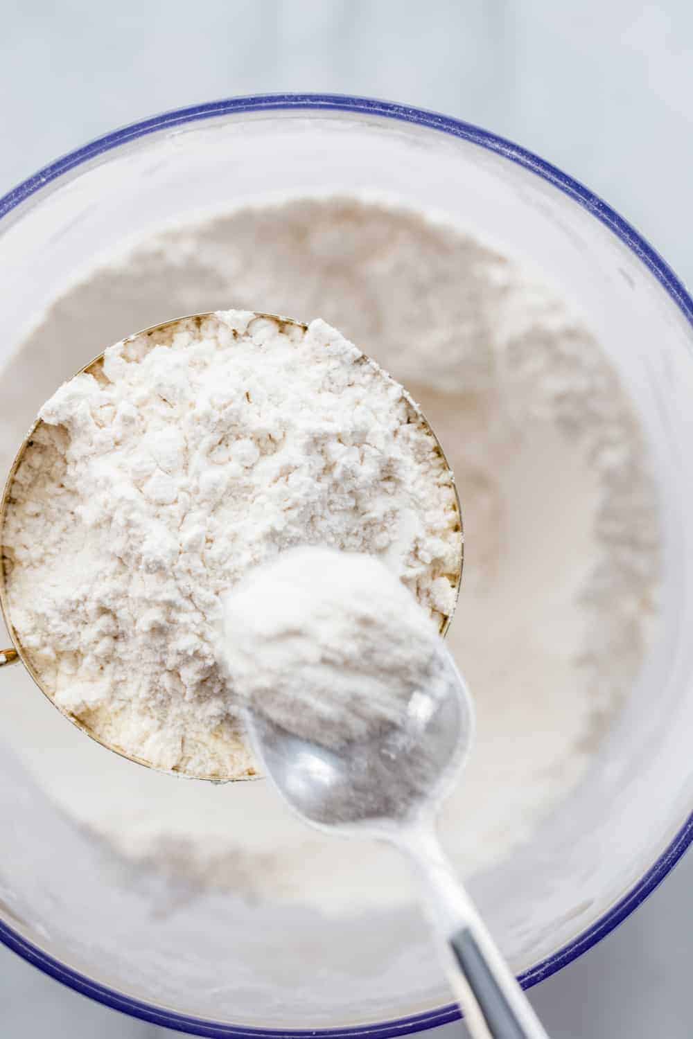 Silver spoon spooning flour into a brass measuring cup over a bowl of flour