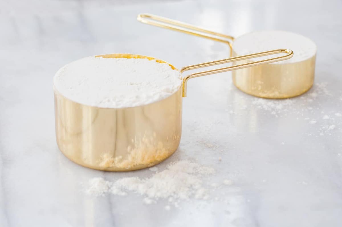 Two gold measuring cups filled with flour on a marble countertop