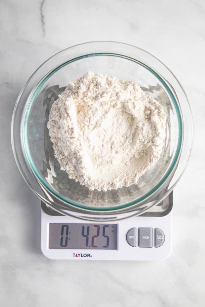 1 cup of flour in a glass bowl being weighed on a food scale. The scale shows 4.25 ounces.