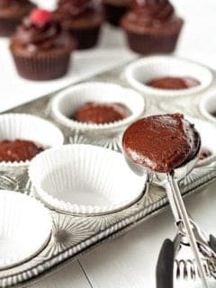 Chocolate muffin batter in a large scoop going into a muffin pan to be baked