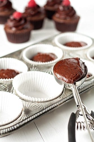 Chocolate muffin batter in a large scoop going into a muffin pan to be baked