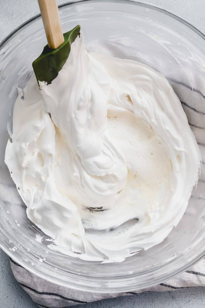 Spatula folding whipped topping into the filling for no bake oreo cheesecake in a glass mixing bowl