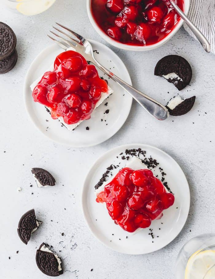 Overhead view of 2 plated slices of no bake oreo cheesecake topped with cherry pie filling with broken oreos scattered around them