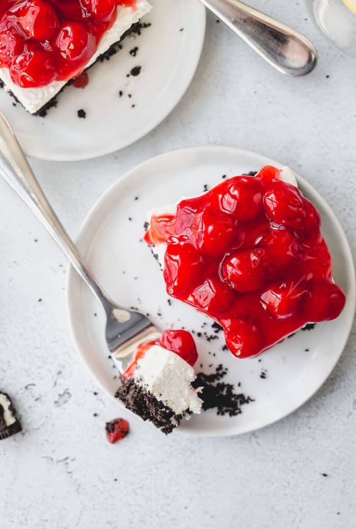 Overhead view of no bake oreo cheesecake topped with cherry pie filling on a white plate next to a fork