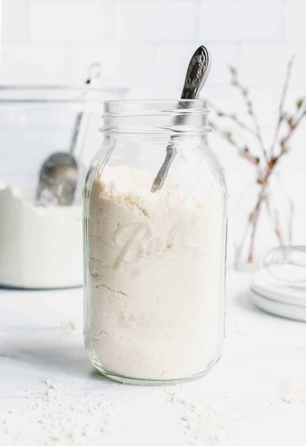 Glass jar of homemade bisquick mix on a white countertop in front of a canister of flour