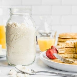 Jar full of homemade bisquick mix next to a stack of homemade pancakes