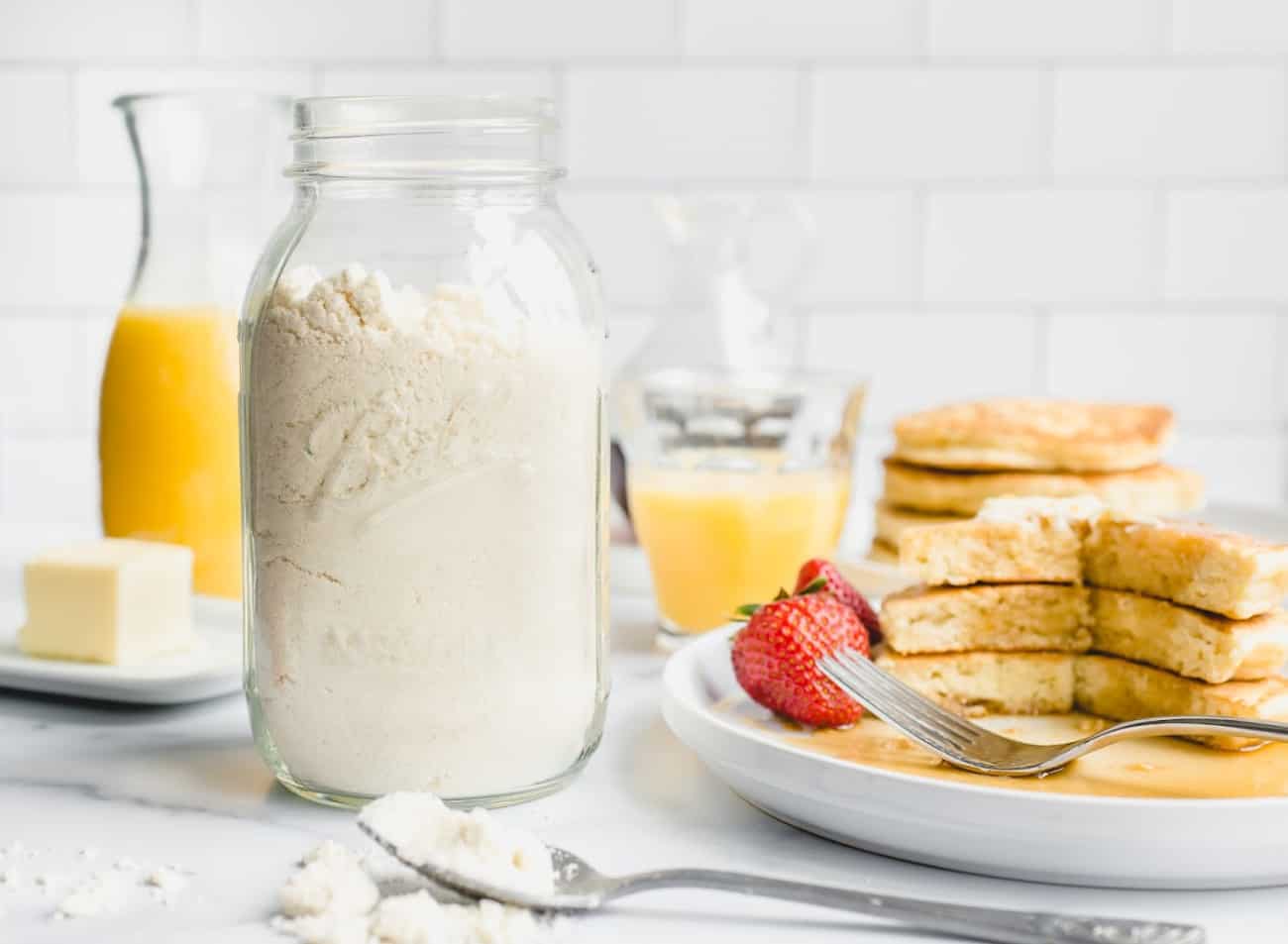 Jar full of homemade bisquick mix next to a stack of homemade pancakes